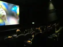 Photo d'une salle de cinéma encore éclairée en pleine projection d'un match de football en haute définition.