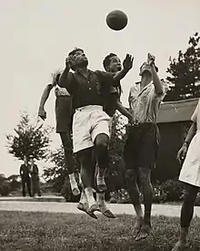 Photographie en noir et blanc de plusieurs joueurs pieds nus s'élevant en l'air pour prendre le ballon de la tête.
