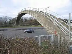 Photo d'une arche en béton avec des marches et des barrières de sécurité qui passe au-dessus d'une route à plusieurs voies sur laquelle circule une voiture