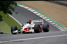 Photo d'une monoplace de Formule 1 blanche et rouge, vue de trois-quarts, dans son ensemble, roulant sur un circuit.