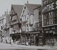 Ancienne photographie du bâtiment Tudor en bois et ses étages supérieurs en sailie.