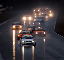 File de voitures zigzaguant sur une piste très mouillé et sous une pluie battante.