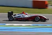 Photographie d'une monoplace de Formule 3 blanche et rouge, vue de profil.