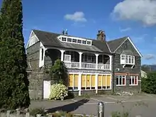 Exterior of two-story building of grey stone with large windows and white wooden balcony on upper floor