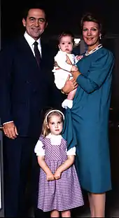 Photographie en couleurs d'un couple et de leurs deux enfants. L'homme porte un costume et la femme une robe bleu. Un bébé se trouve dans les bras de la femme et une petite fille est entre le couple.