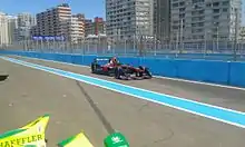 Photographie d'une monoplace de Formule E noire, dans les stands, sous un grand ciel bleu.