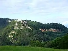 Photographie en couleurs d'une montagne recouverte de végétation sur laquelle se trouvent un fort militaire et un affleurement rocheux.