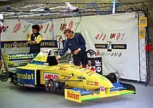 Photo d'un garage dans lequel se trouve une monoplace jaune et deux personnes