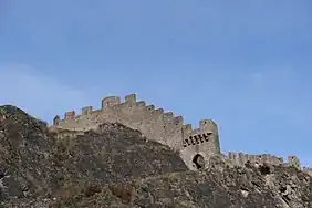 Mur en pierres crénelé suivant le contour d'un rocher.