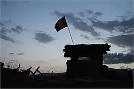 Un drapeau flotte au-dessus d'un tour militaire devant un ciel sombre.