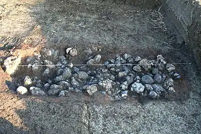 Lit de pierres calcaires et auréole de terre rubéfiée signant un four enterré.