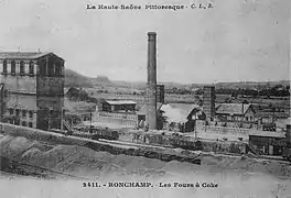 Un haut bâtiment industrielle sur la gauche, d'autres plus petit à droite surmontés d'une haute cheminée.