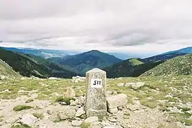 Photographie d’une borne, sur fond de montagnes.