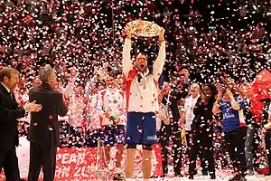 Fernandez brandissant le trophée de l'Euro 2010 devant le reste de l'équipe de France et sous les confettis.