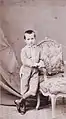 Photographie ancienne d'un petit garçon en costume, accoudé à un fauteuil.