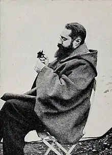 Portrait de Francis Jammes assis, vu de profil, observant une fleur.