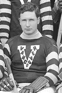 Photographie en noir et blanc d'un joueur de hockey assis avec un V sur le maillot, V dans lequel est inscrit VANCOUVER
