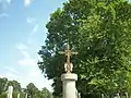 Monument avec une croix en fer forgé. Sur la croix est représentée l'Assomption de Marie, à la base, deux anges en prière