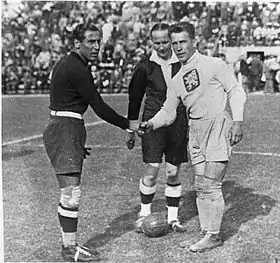 Juste avant le match, deux joueurs se serrent la main devant l'arbitre. Ils sont de face.