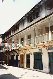 Grande maison en longueur d'aspect vétuste, avec des murs blancs, deux étages, de nombreux balcons et fenêtres.