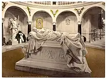 Photographie en couleur d'un gisant d'homme placé au milieu d'une pièce de forme ronde.