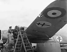 Photo en noir et blanc de mécaniciens changeant un moteur sur un avion frappé de la Croix de Lorraine bleue et de la cocarde tricolore.