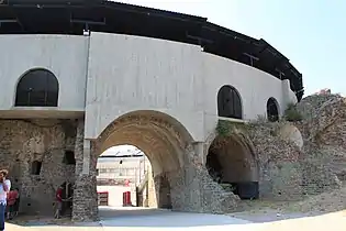 Entrée du monument : les vestiges romains sont traversés par des piliers et des murs de béton. Des tôles coiffent les parties extérieures.