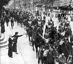 Photo en noir et blanc d'une colonne de cavaliers portant casque et cuirasse, salués par les civils.