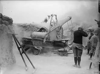 Photo noir et blanc d'un gros canon venant de tirer, dans un nuage de poussière.