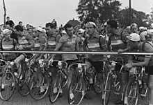 Photographie en noir et blanc montrant des coureurs d'une même équipe alignés devant le peloton avant le départ d'une course.