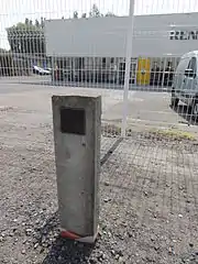 Photographie de la petite borne en béton armé indiquant que l'avaleresse Point du Jour se situe trois mètres derrière, sur le parking d'un concessionnaire Renault. Cette avaleresse est un des premiers puits du bassin minier hors Boulonnais.