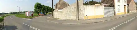 Panorama réalisé à Fresnes-sur-Escaut montrant la rue et les habitations. Une petite borne en béton apparaît le long d'un mur, il s'agit d'une tête de puits non matérialisée indiquant que le puits Jeanne Colard no 1, creusé en 1718 et abandonné en 1721, se situe quelques mètres derrière.
