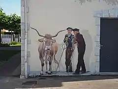 Photographie en couleurs d'une peinture sur un mur, représentant une vache et deux hommes.