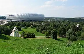 Fröttmaninger Berg, à gauche l'installation artistique « Village englouti », à droite l'église Heilig-Kreuz (de), à l'arrière l'Allianz Arena.