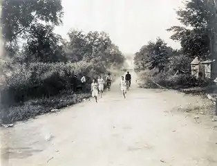 Trois hommes habillés en blanc sur une piste de terre, suivis par des vélos.