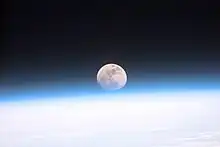La Lune est visible au-dessus de la Terre et son atmosphère bleutée, formant un disque légèrement aplati.