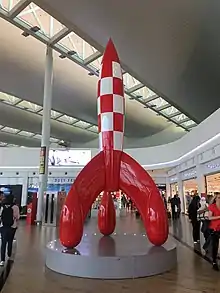 Photographie couleur d'une reproduction de fusée rouge et blanche dans le hall d'un aéroport.