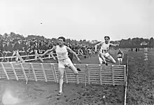 Photographie en noir et blanc de coureurs à pied sautant une haies.