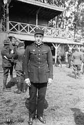 Photographie en noir et blanc d'un homme debout en tenue militaire à l’extérieur d'un bâtiment.