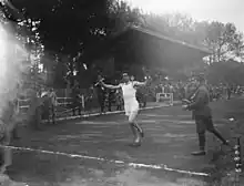 Photographie en noir et blanc d'un coureur à pied à l’arrivée d'une course dans un stade.