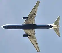 Vue de dessous d'un avion à réaction en vol. Un moteur est accroché à chacune des deux ailes. L’empennage horizontal est à l'arrière.
