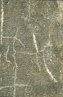 Photographie de la surface plane d'une pierre sur laquelle des gravures de caractres chinois sont visibles.