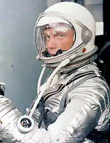 Glenn dans une combinaison spatiale argentée, avec son casque et sa visière transparente baissée.