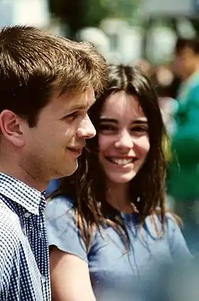 Une jeune fille brune souriante, cheveux longs et yeux sombres, de face, et un jeune homme de profil