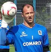 Gardien de but de football avec un maillot bleu, portant un ballon, vu de face