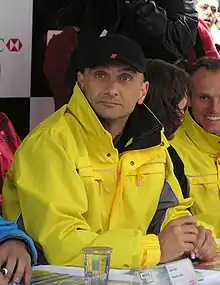 Photo d'un homme assis, portant une casquette noire et un vêtement jaune