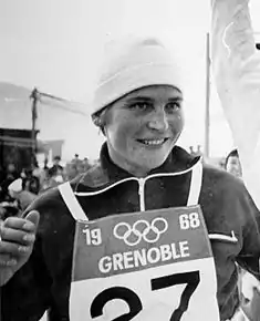 Photographie en noir et blanc d'une athlète portant un dossard marqué Grenoble 1968 et les anneaux olympiques.