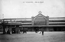 Carte postale en noir et blanc avec la gare de départ, un kiosque et des personnages.