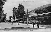 La cour extérieure de la gare, avec le bâtiment voyageurs et les voitures et omnibus en attente, vers 1900