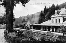 Voies, quai, bâtiment voyageurs et arrivée d'un train avec une locomotive à vapeur